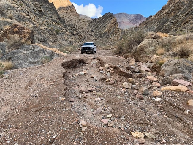 A Park Ranger truck parked at a large washout in a dirt road in a desert canyon.