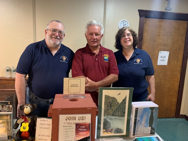 Three people standing at a table with decorations and information about the park on it.