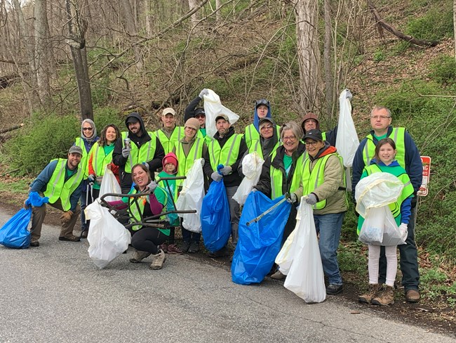 A group of volunteers in safety vests hold trash bags and pose for a picture.