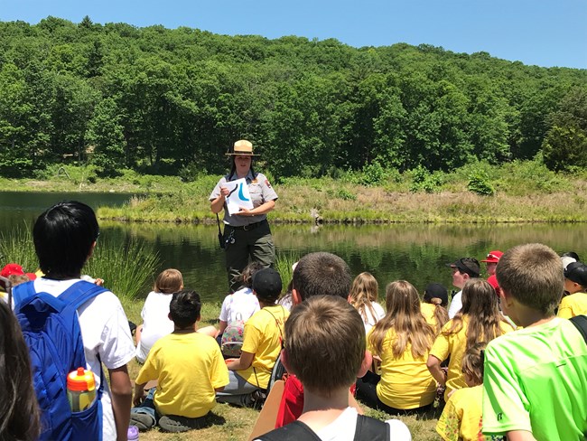A group of students listening to a ranger while sitting outside.