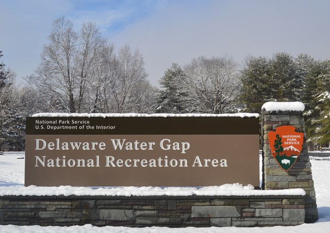 The DEWA Entrance sign covered in snow and in front of a field of snow.