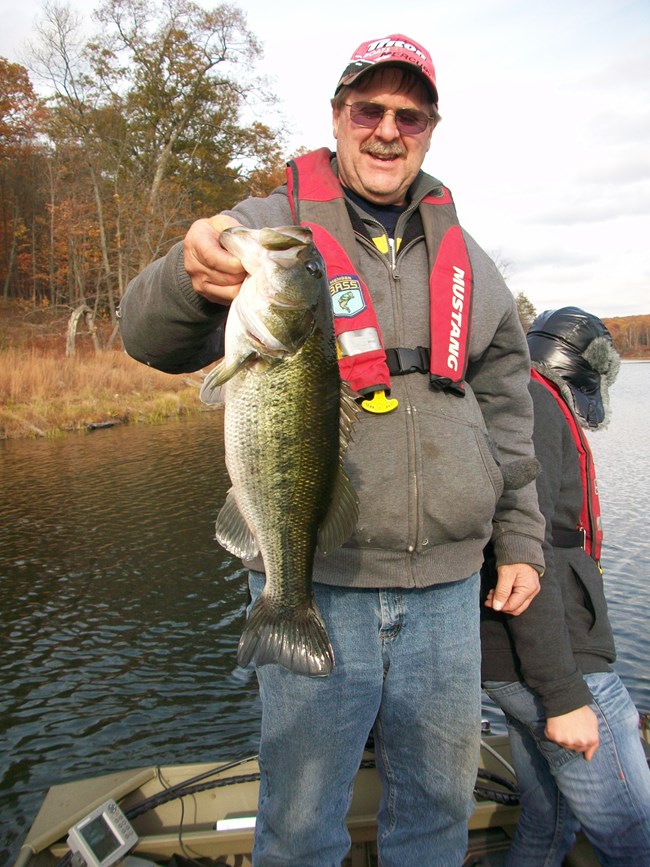 Image of a fisherman in a baseball hat standing in a bass boat and holding a large mouth bass
