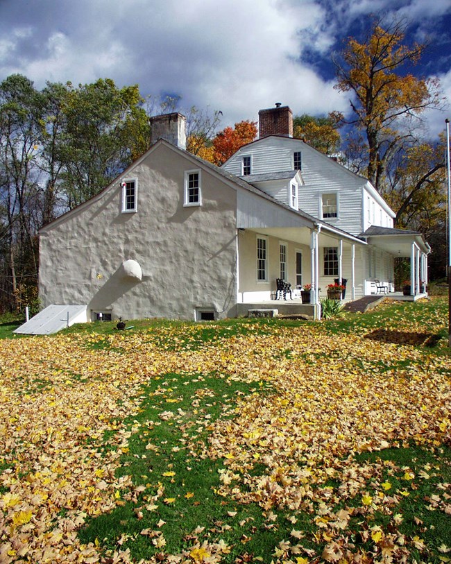 White house with fallen leaves covering a green yard.