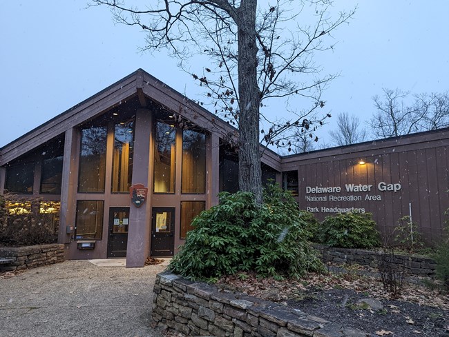 A brown craftsman style building with snow flurries coming down around it.