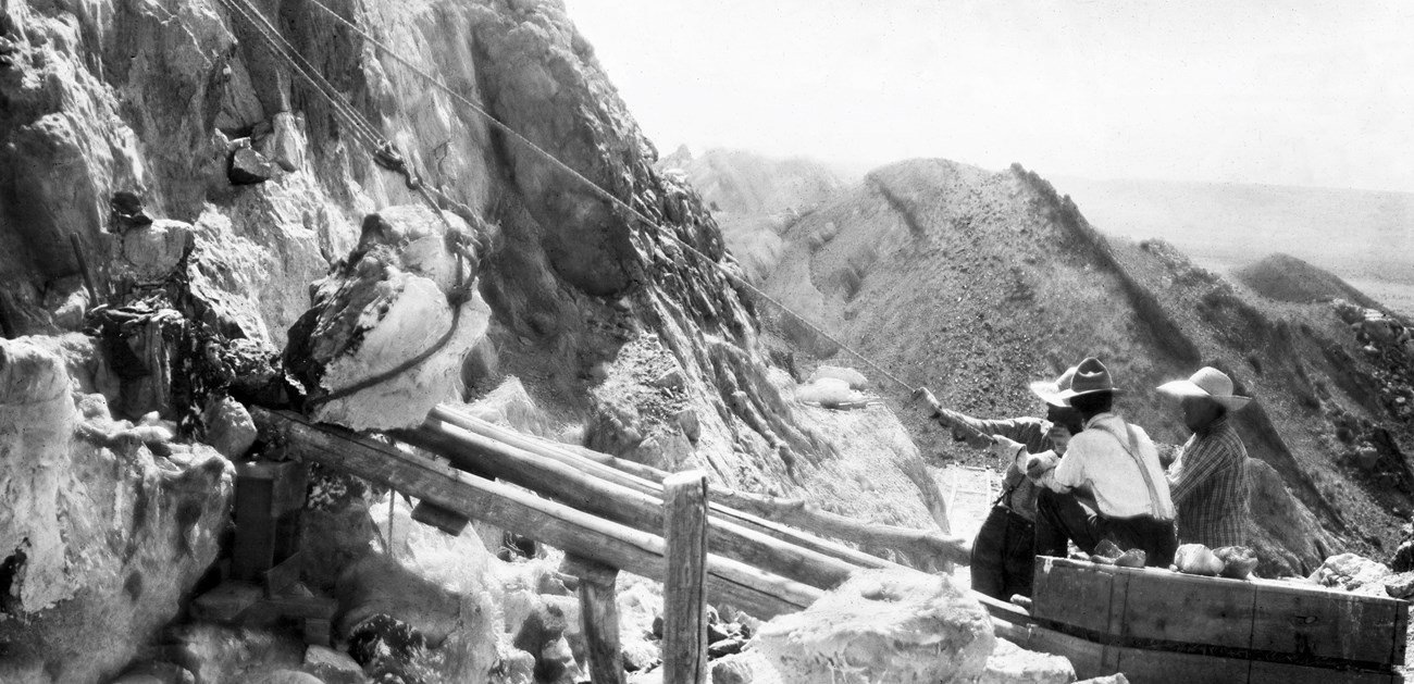 A black and white photograph of some people at the original Carnegie Quarry dig site. They are using a pulley system to extract a fossil from the rock face.