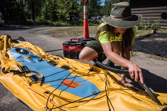A ranger vacuums excess water out of a yellow inflatable kayak.