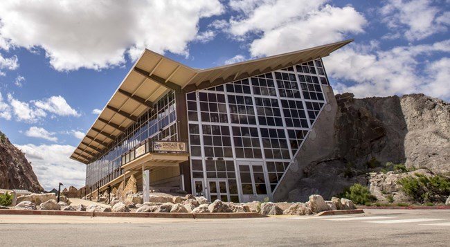 The Quarry Exhibit Hall as it appears today from the parking lot. It's a large glass building with a sloping roof built into the side of a rock face.