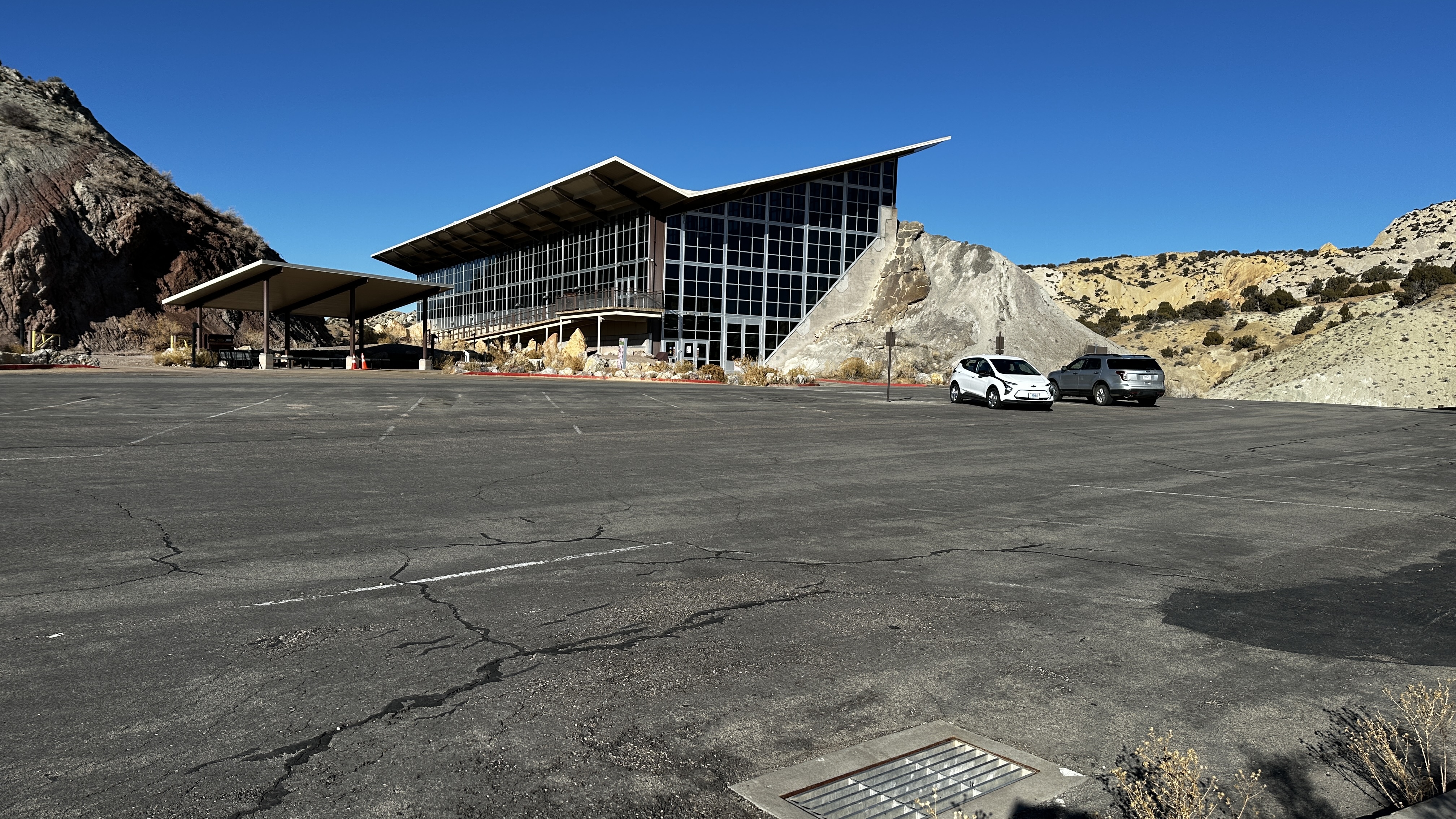 Parking lot in front of building with angled roof under a blue sky.