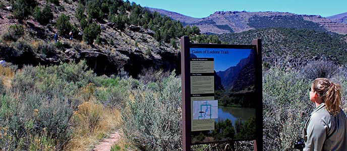 A visitor reads a trailhead sign for the Gates of Lodore trail.