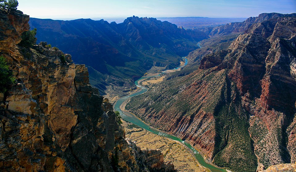 Green colored river flowing in canyon between two mountains made of multi-colored rocks.