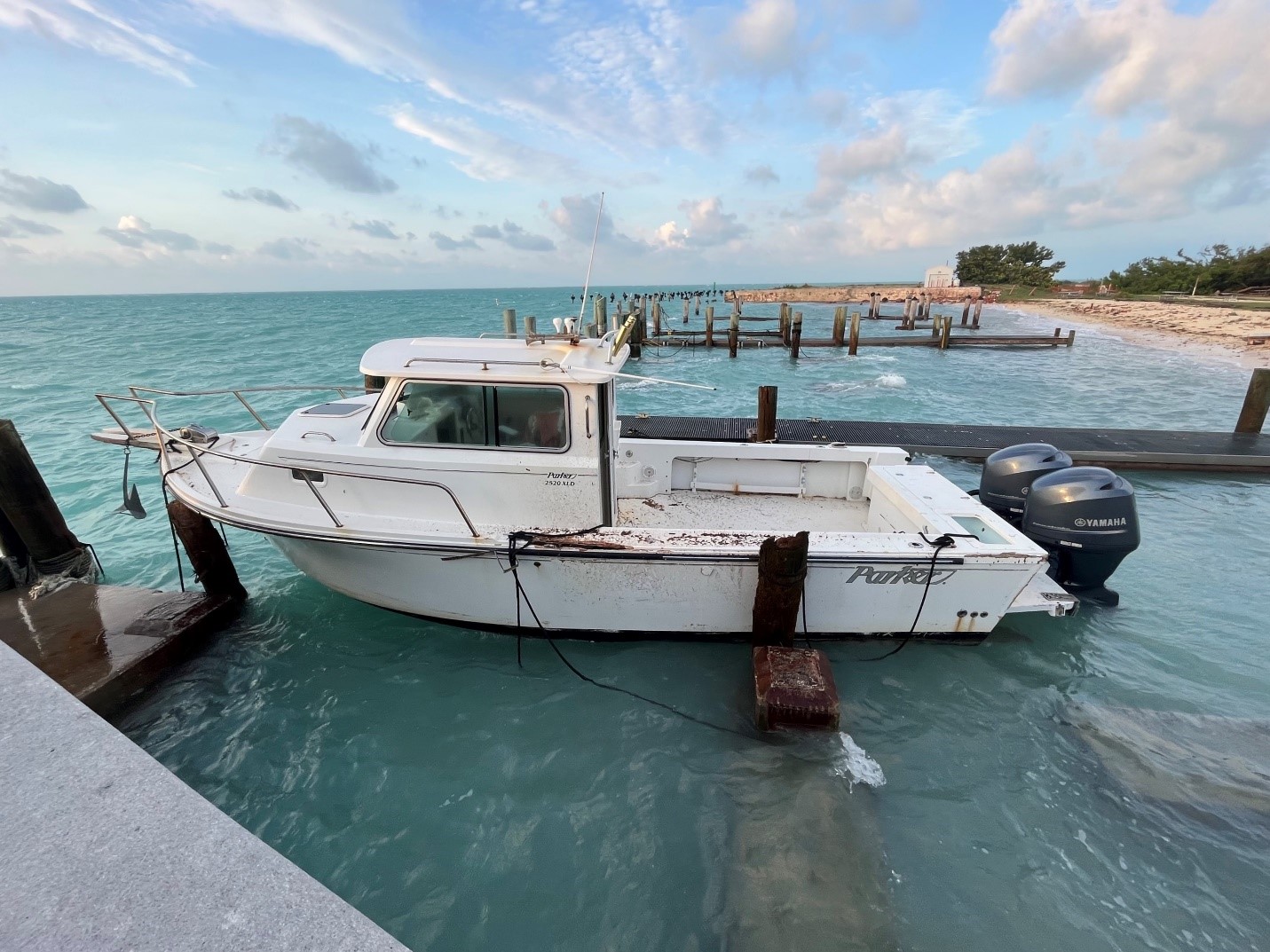 A white boat damaged during a hurricane sits in the water tied to a dock
