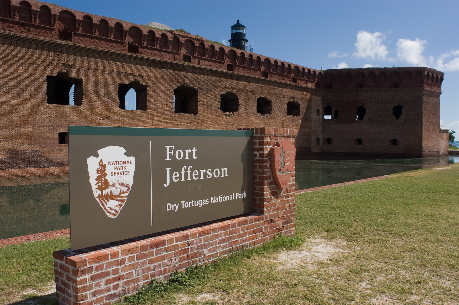 A sign in front of a large brick structure, showing the National Park Service arrowhead and the words "Fort Jefferson Dry Tortugas National Park"