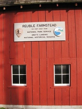 Side of red barn with sign and two windows.