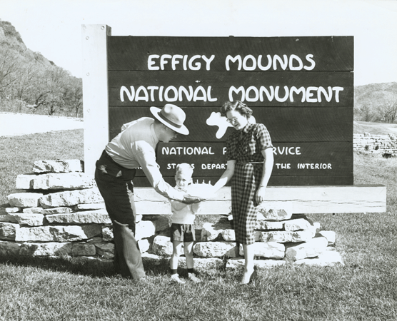 Holding cake in front of Effigy Mounds sign