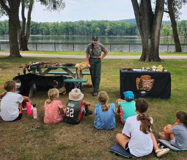 Image of a ranger giving an animal program to a group of children outside.