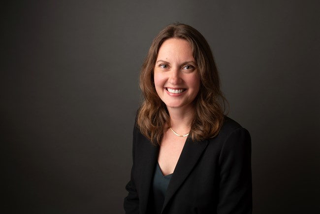 A woman in a dark suit smiles at the camera