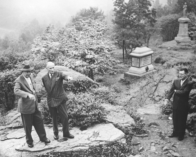 A black and white image of two men standing on a rock and pointing