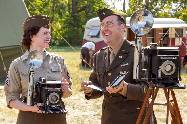 An image of two living history volunteers in WWII uniforms smiling for the camera