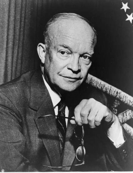 President Eisenhower is holding his glasses, while glancing off to the side with a furrowed brow