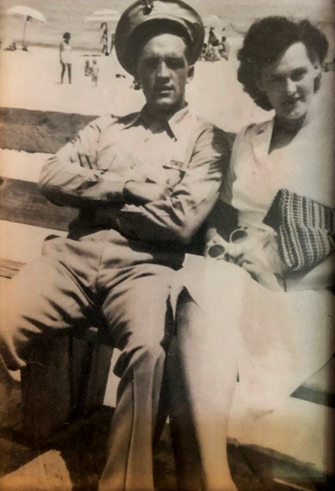 A black and white photo of Thomas Lindsay in him military uniform sitting on a bench with a woman at the beach..