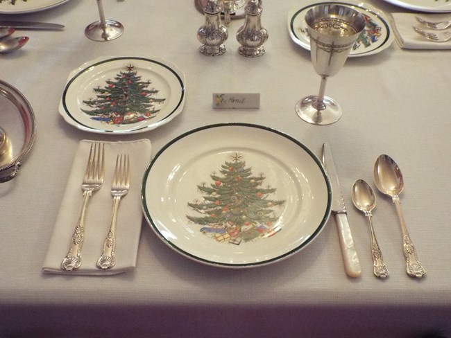Mamie's Christmas china plates on a white tablecloth with silverware and drinkware around them
