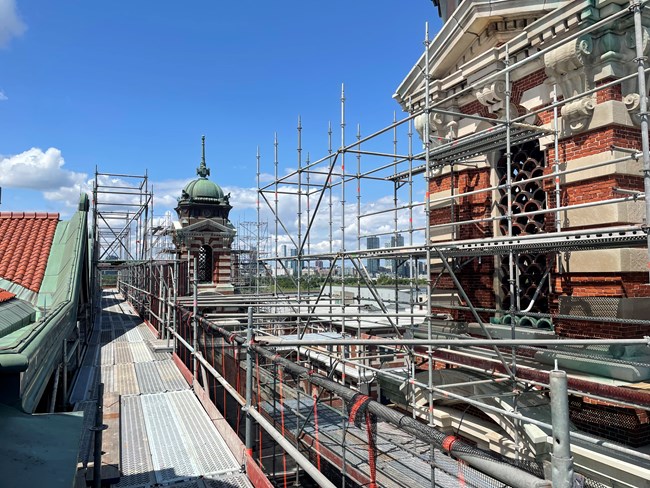 Scaffolding surrounds a brick building with ornate towers visible