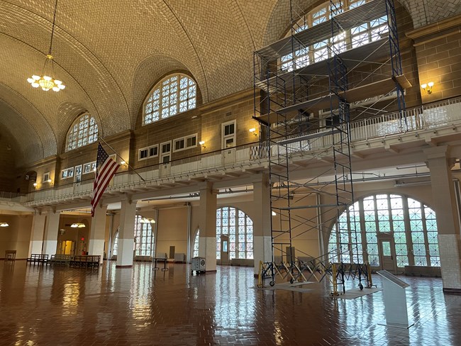 A photo of a large hall with a vaulted ceiling and large, semicircle windows. There is scaffolding that goes from one floor up to the level above.