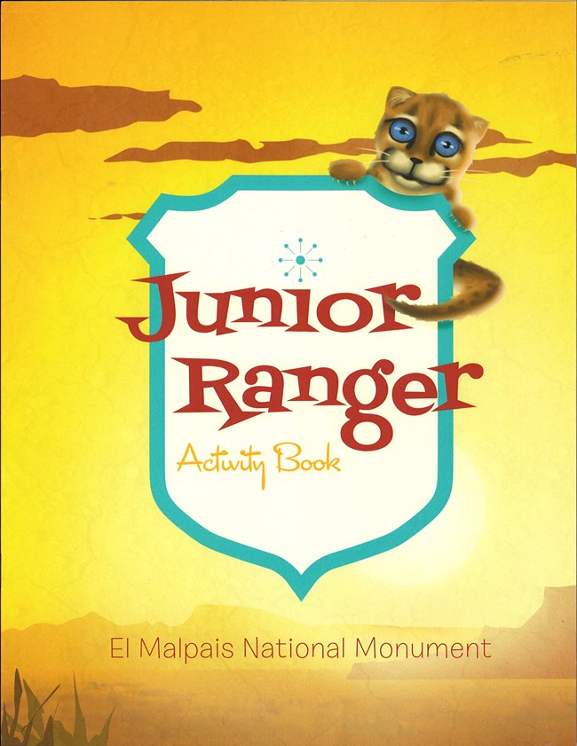 A blue-eyed cat holds a "Junior Ranger Activity Book" logo in front of a yellow sunset.