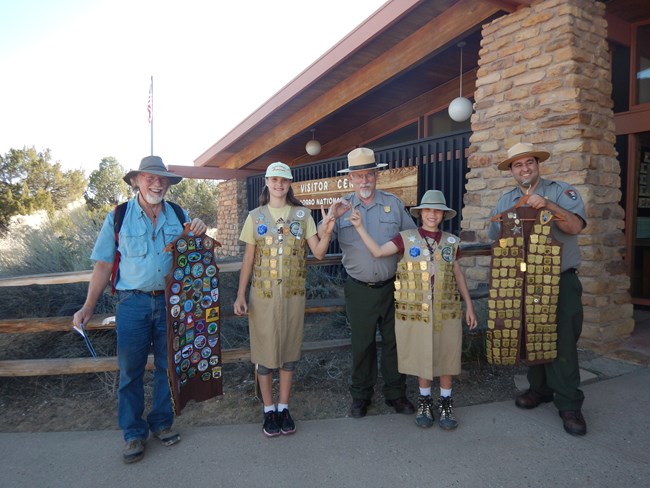 Junior Rangers stand with Park Rangers displaying four vests covered in badges.