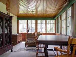 An enclosed porch with bed, carpet, table, and chairs.