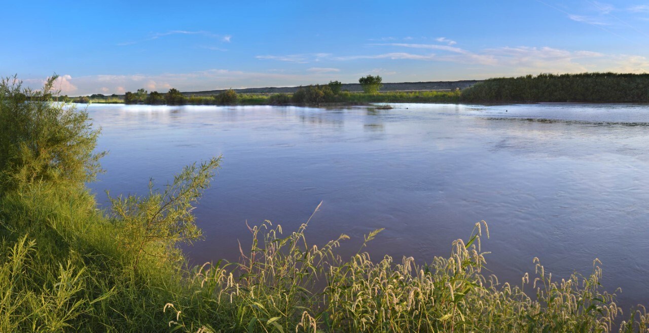 Un río ancho, tranquilo fluye entre riberas cubiertas en hierba verde y baja