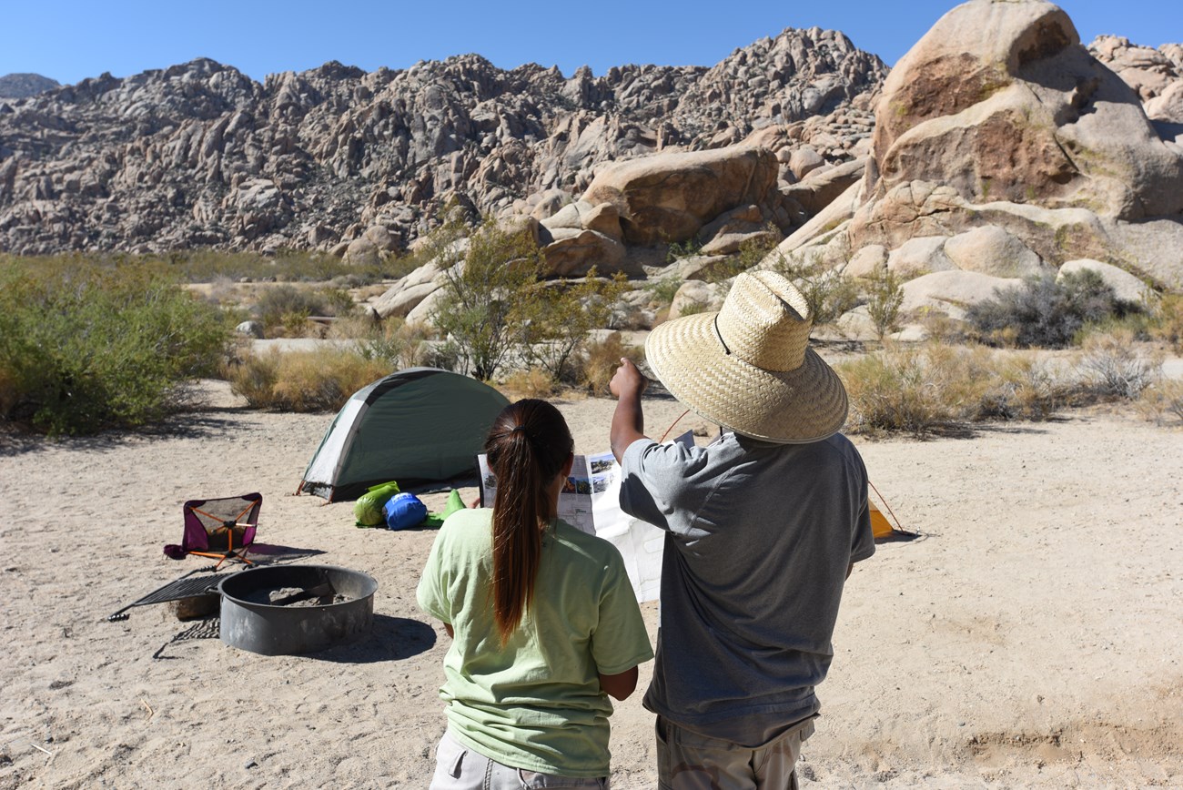 Dos visitantes en su sitio de campamento con una carpa, sillas alrededor de rocas de granito.