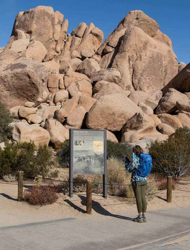 Park visitor reading information board with boulders in the background.