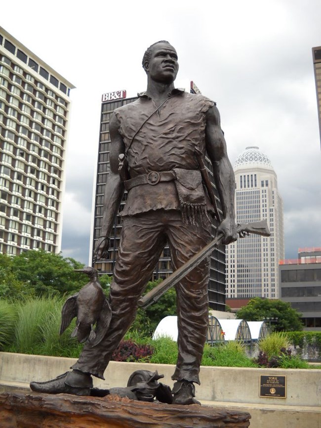 A bronze statue of York In downtown Lousiville Kentucky holding a rifle and a duck