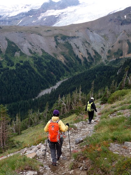 Dos excursionistas caminando en un sendero que desciende hacia un frondoso valle.