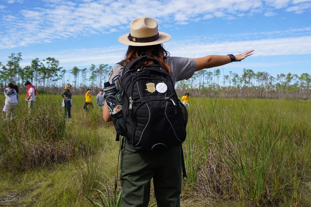 A Park Ranger stands in front of a group of students while pointing.