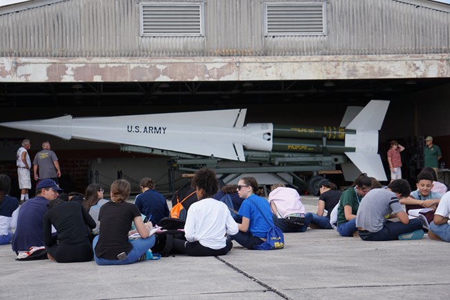 Students sitting and reflecting in front of a large Nike Missile