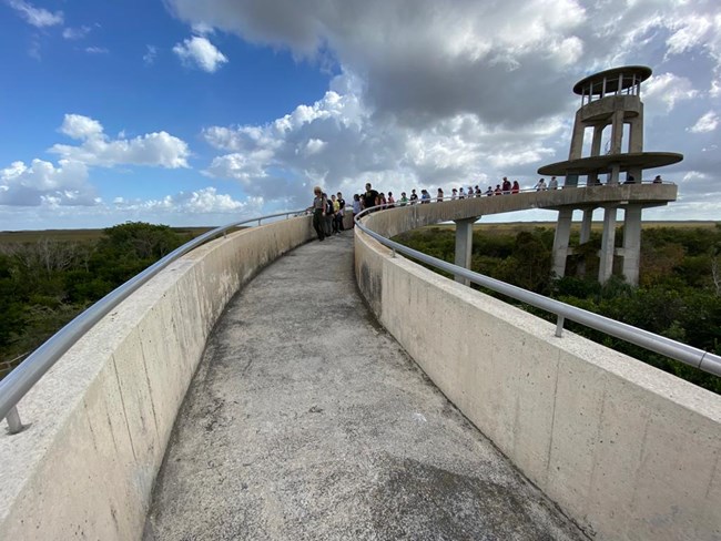 People walking up a cement ramp towards a tower