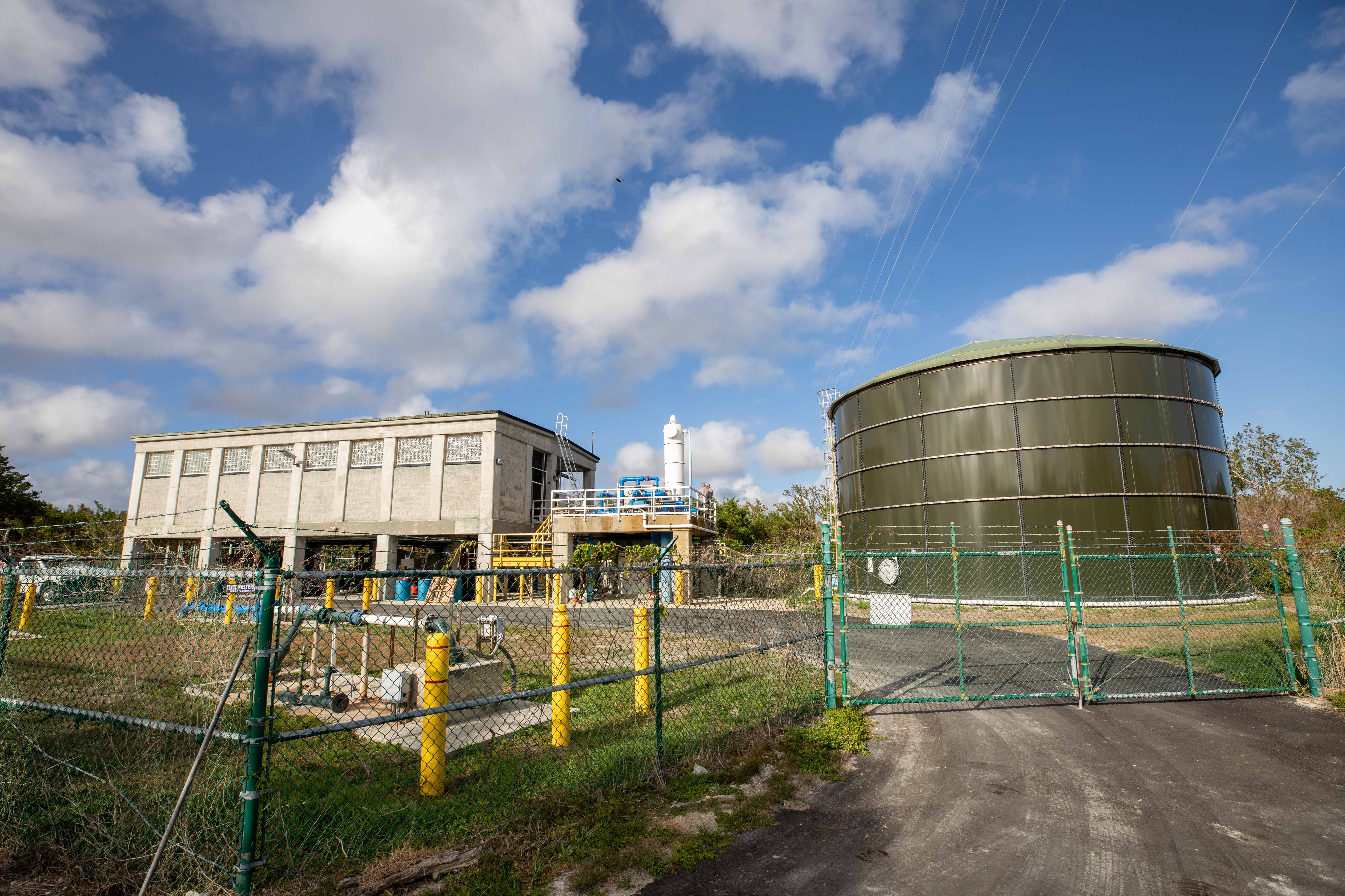 Large water tank, elevated concrete building and outdoor pipes behind a fence