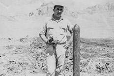 Man in hat posing next to survey marker pole, desert landscape in the distance. 