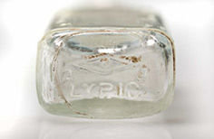 Bottom of aged clear glass medicine bottle with imprinted markings.