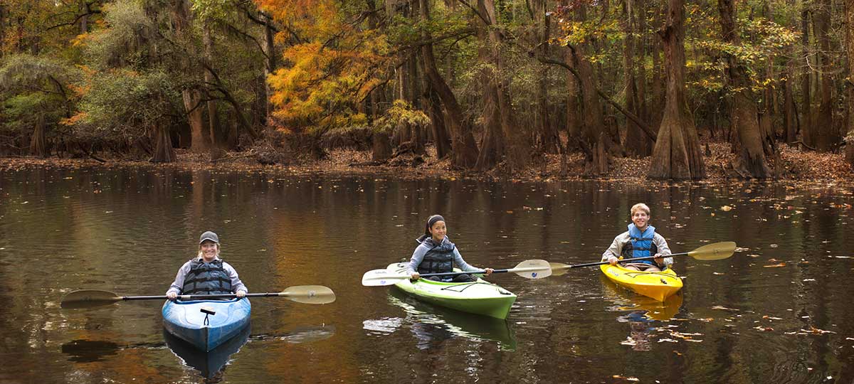 three people kayaking on a river in autumn