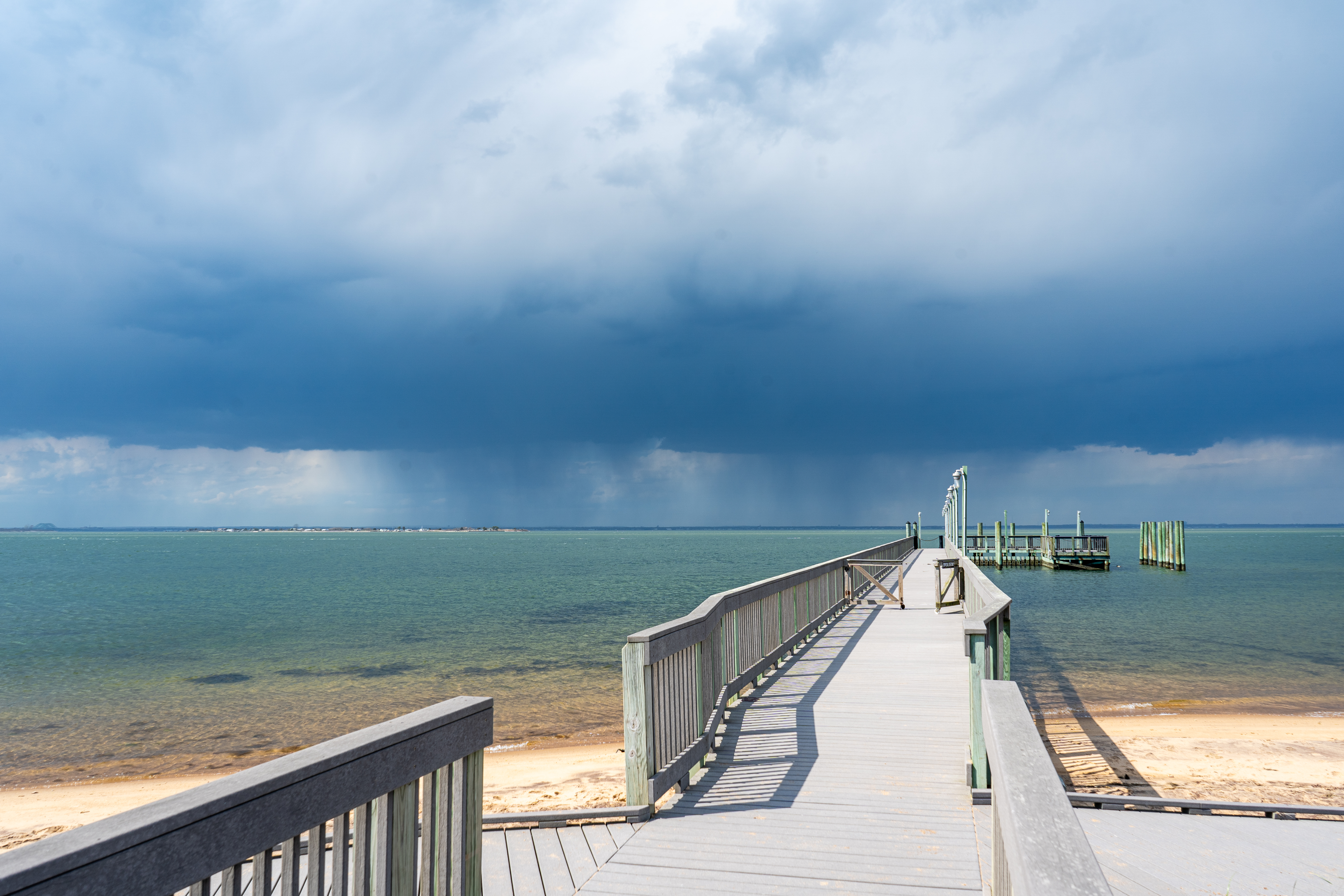 A view of a dock and calm bay waters with dark rain clouds in the distance.