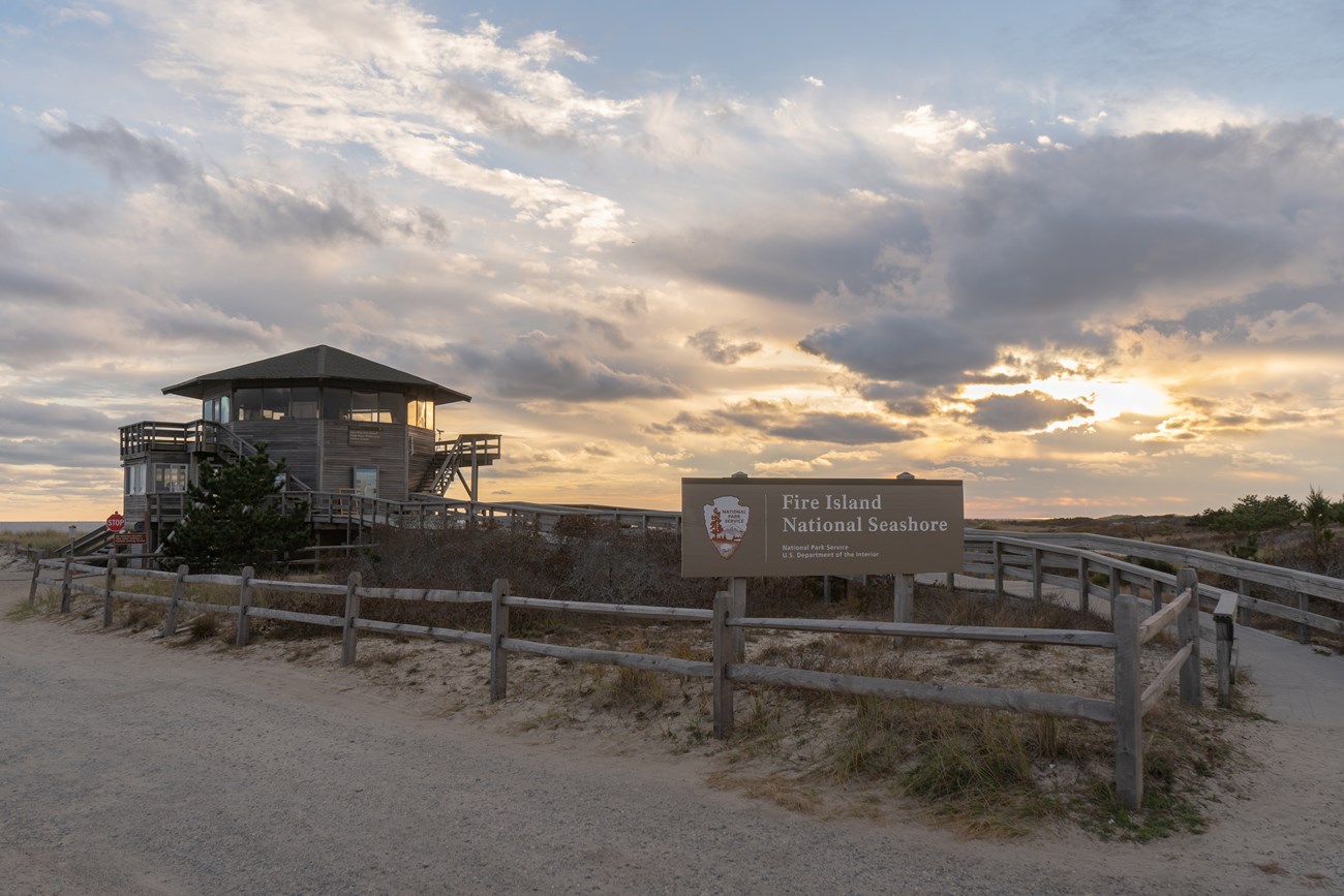 A wooden building and sunset with sign displaying "Fire Island National Seashore."