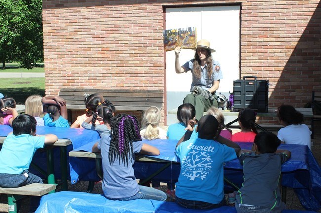 A park ranger presenting a Read with a Ranger program to a group of young students outside.