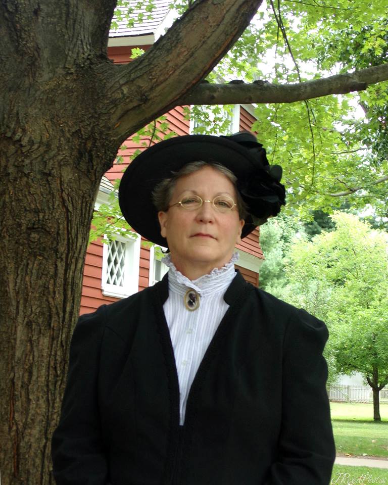 Living history interpreter Debbie Weinkamer dressed as widow Lucretia Garfield, stands next to a tree on the grounds of James A Garfield NHS