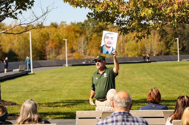 A volunteer holds an image of a passenger from Flight 93 while talking to a group of visitors