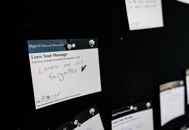 Tribute cards posted on black wall at Memorial Plaza shelter