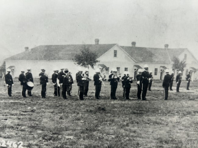 Several men in uniform play intsruments together in front of a building, highlighting their coordinated outfits.