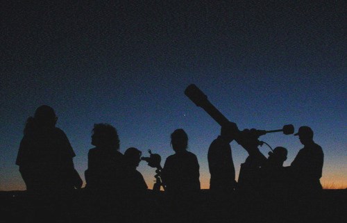 A group of people gathered around a telescope, observing the night sky filled with stars.
